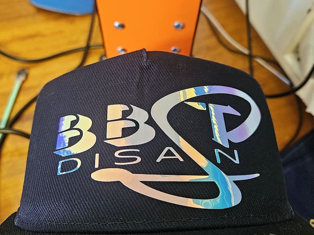Must nokamüts BBST Disaini holograafilise logoga mütsipressi ees